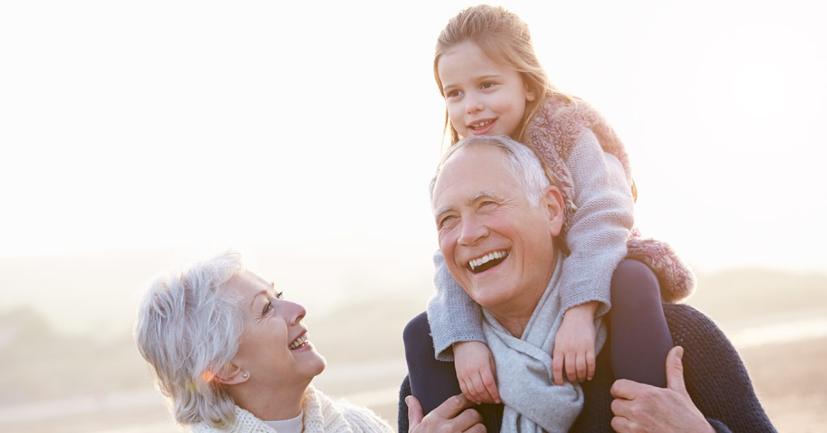Großeltern lachen mit Enkelin auf den Schultern des Opas am Strand | Immobilienverrentung